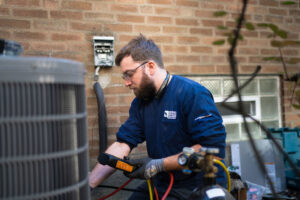 An HVAC technician diagnosing an outdoor air conditioning unit with a tool for Alan Energy Services in Naperville, IL
