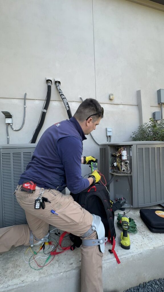 An HVAC technician diagnosing an outdoor AC unit with a multimeter for Bree HVAC Contractor in Cedar Park, TX.