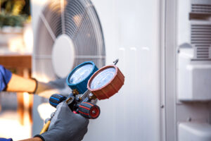 An HVAC technician diagnosing an outdoor AC unit with a digital manifold gauge for Taylor & Tyler HVAC, New Orleans, LA.