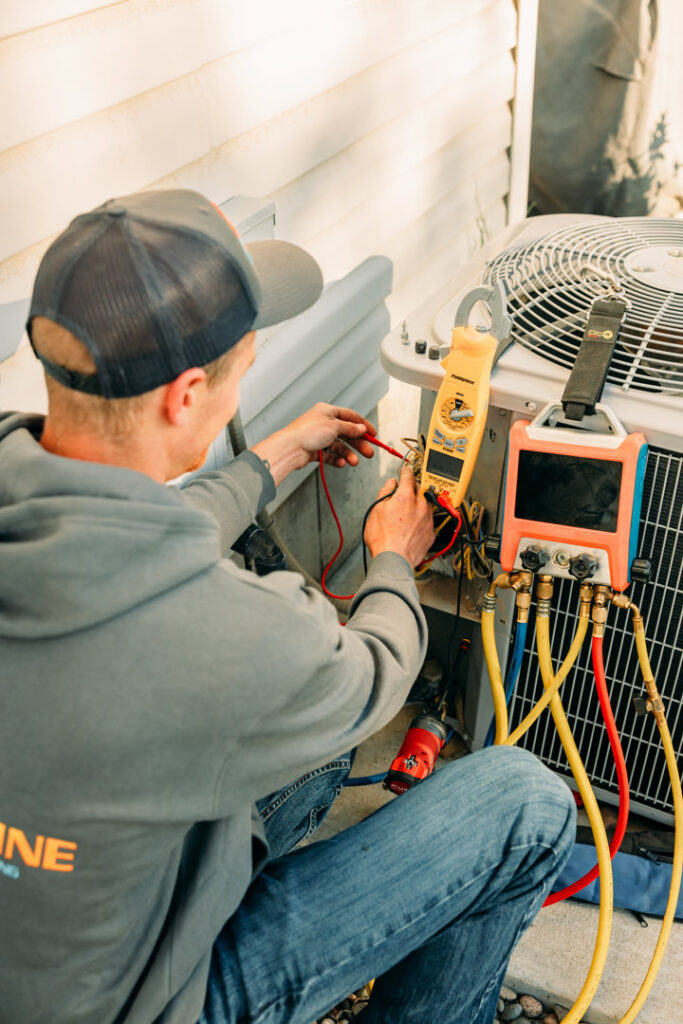 An HVAC technician diagnosing an outdoor air conditioning unit with specialized tools for Ridgeline Heating and Cooling in Idaho Falls, ID.