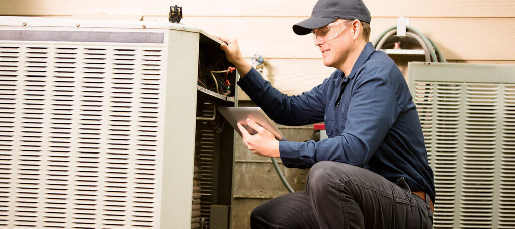 An HVAC technician diagnosing an outdoor air conditioning unit with a tablet for Baker Heating & Cooling in Dayton, OH.
