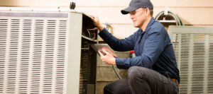 An HVAC technician diagnosing an outdoor air conditioning unit with a tablet for Baker Heating & Cooling in Dayton, OH.