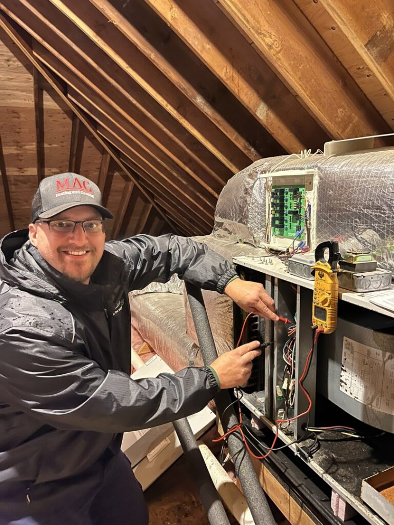 An HVAC technician from MAC Heating and Cooling LLC diagnosing an air handler unit in an attic in Waterbury, CT.