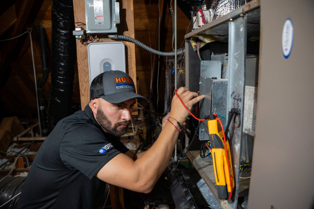 An HVAC technician diagnosing a furnace or air handler in an attic for Hurn Mechanical Heating & Cooling in El Cajon, CA.