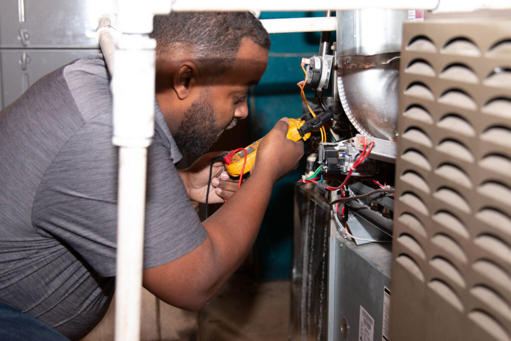 An HVAC technician from Nashville Solutions diagnosing an indoor furnace or air handler unit with a multimeter in Nashville, TN