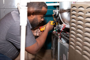An HVAC technician from Nashville Solutions diagnosing an indoor furnace or air handler unit with a multimeter in Nashville, TN