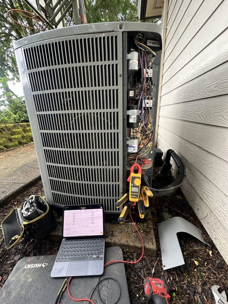 An HVAC technician diagnosing an outdoor AC unit with a laptop at Elevate Heating & Cooling in Hillsboro, OR.