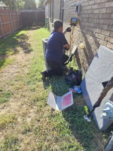 An HVAC technician kneeling and diagnosing an outdoor AC unit with a tool for MasterCraft Mechanical, LLC. in Haslet, TX.