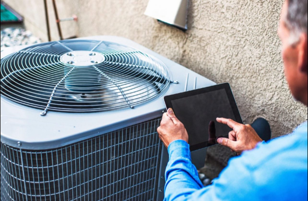 An HVAC technician using a tablet to diagnose an outdoor air conditioning unit for My Mechanical Heating and Cooling in Lancaster, PA