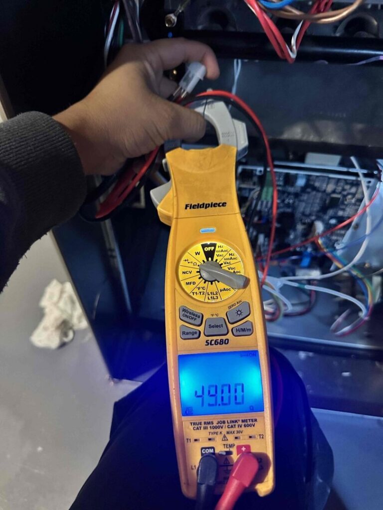An HVAC technician using a clamp meter to diagnose an HVAC unit's electrical system for Markool Heating Cooling Plumbing in Frederick, MD.