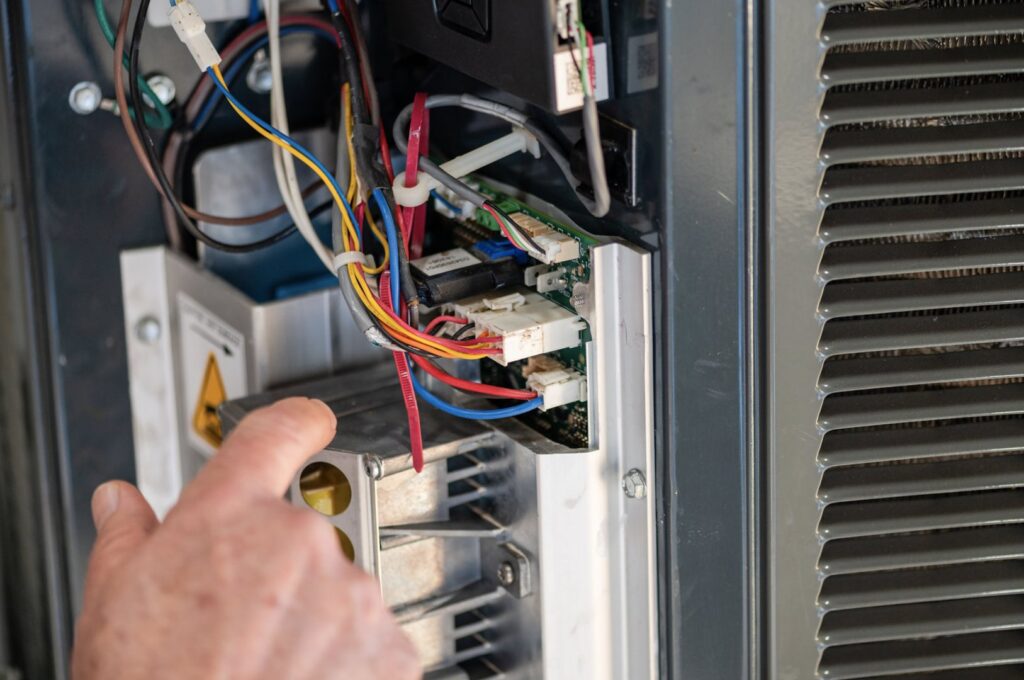 An HVAC technician from DFH Company Heating and Air Conditioning diagnosing wiring and circuit boards inside an HVAC unit in Louisville, KY.