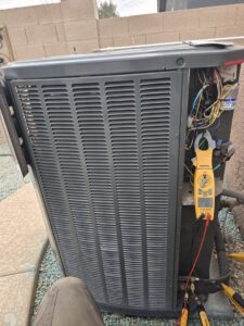 An HVAC technician using a multimeter to diagnose an outdoor AC unit for Quantum Cooling & Heating in Mesa, AZ.