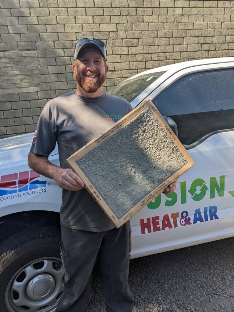 An HVAC technician from Fusion Heat and Air in Fort Smith, AR, holding a dirty air filter during a service call.