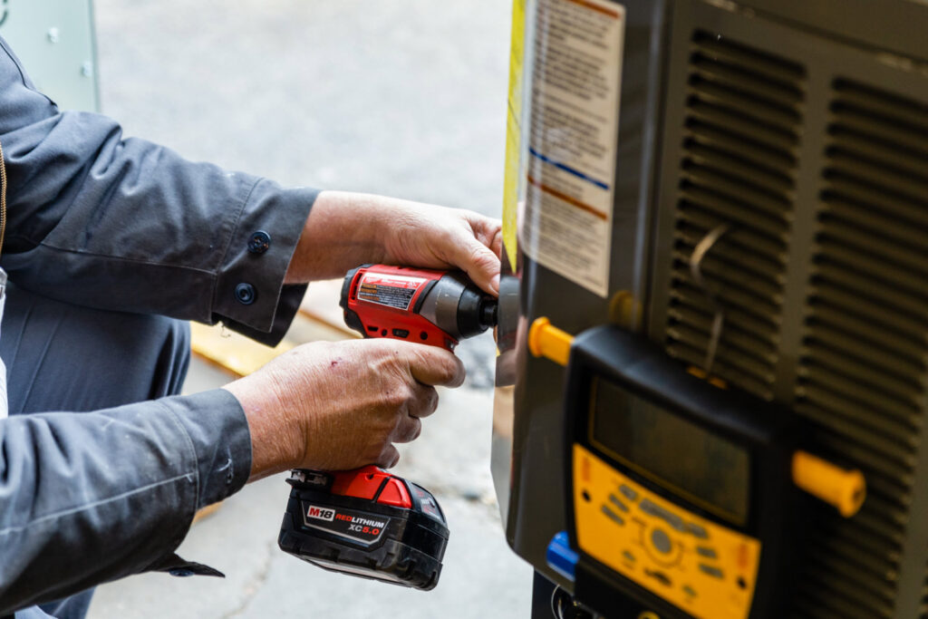 An HVAC technician from DFH Company Heating and Air Conditioning using a power drill on an outdoor AC unit in Louisville, KY.