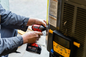 An HVAC technician from DFH Company Heating and Air Conditioning using a power drill on an outdoor AC unit in Louisville, KY.