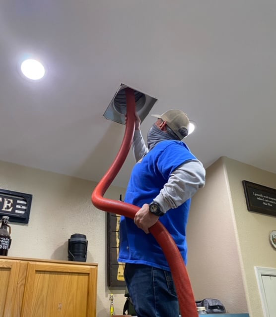 An HVAC technician performing duct cleaning on a ceiling vent for Desert Air Systems in Glendale, AZ.