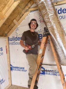 An HVAC technician on a ladder installing ductwork in a new construction home for Southern Comfort Heating/Cooling/Gas in Fayetteville, NC.