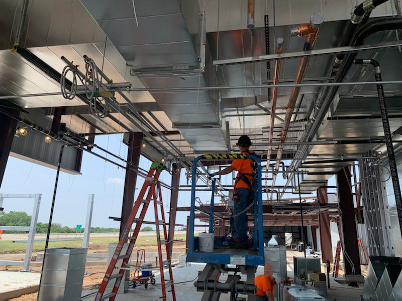 An HVAC technician on a scissor lift installing ductwork and piping in a commercial building by Central Consolidated in Wichita, KS