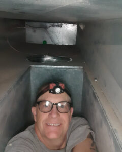 An HVAC technician with a headlamp smiling while inspecting the interior of ductwork for Arrowseal of Billings HVAC in Billings, MT.