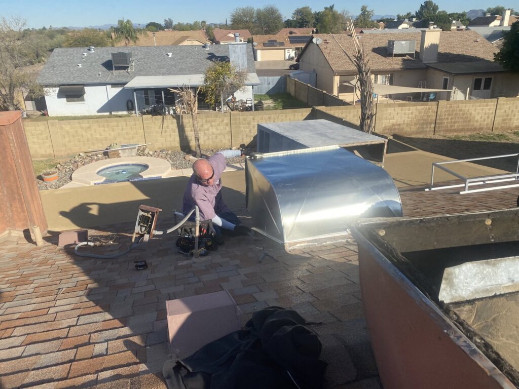 An HVAC technician performing ductwork repair on a residential rooftop for Gotham Air LLC in Glendale, AZ.