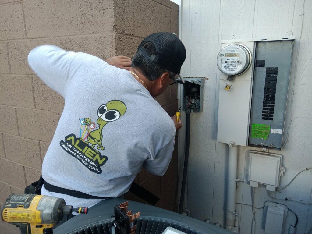 An HVAC technician from Alien Air Conditioning and Heating servicing an electrical panel next to an outdoor AC unit in Phoenix, AZ.