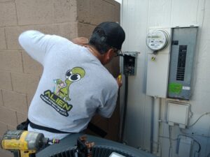 An HVAC technician from Alien Air Conditioning and Heating servicing an electrical panel next to an outdoor AC unit in Phoenix, AZ.