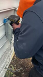 An HVAC technician performing electrical work on an outdoor unit connection for Miller's Home Comfort-Chesapeake in Chesapeake, VA.