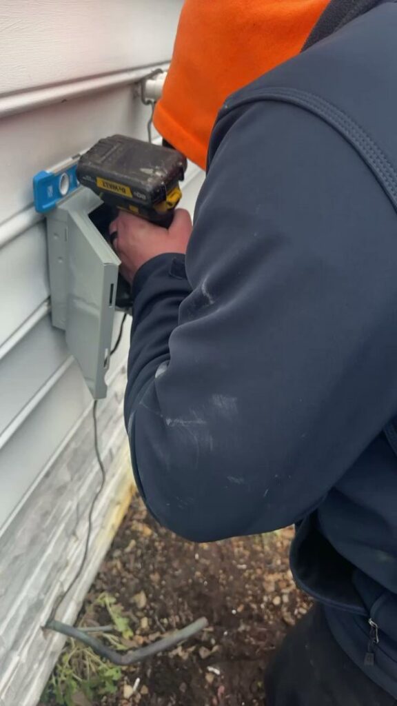 An HVAC technician performing electrical work on an outdoor unit connection for Miller's Home Comfort-Chesapeake in Chesapeake, VA.