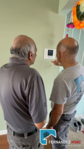 An HVAC technician from Fernandez HVAC explaining a smart thermostat to a customer in Alexandria, VA.