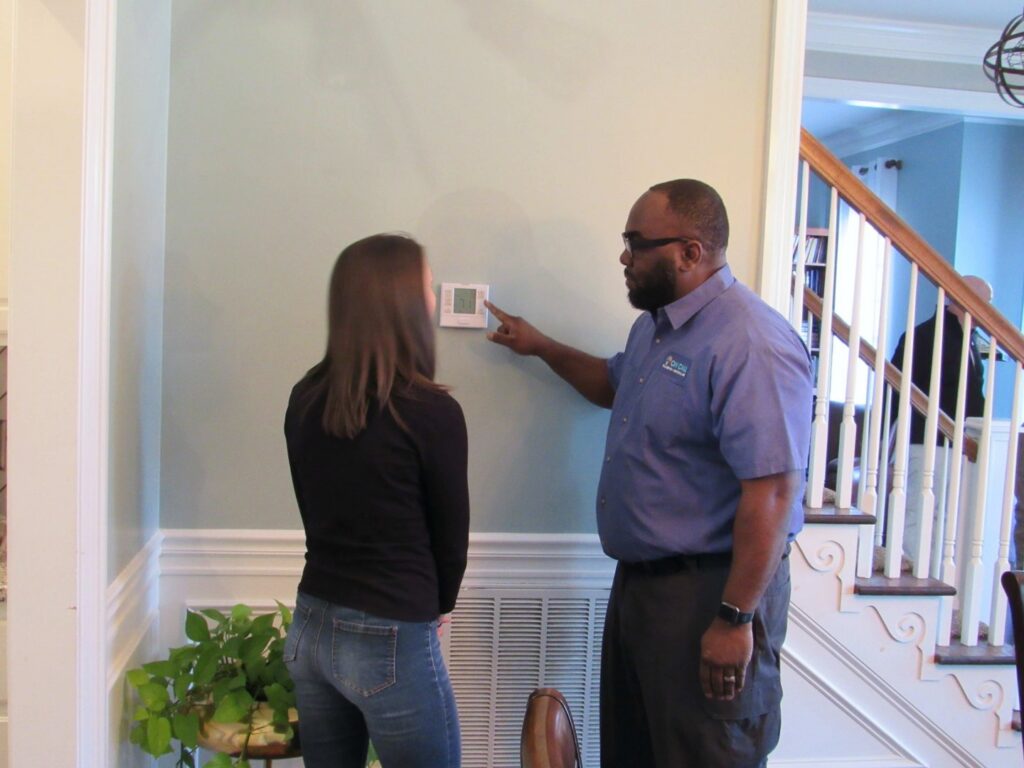 An HVAC technician explaining a thermostat to a customer in a home by On Call Plumbing, Heating & Air in Columbia, SC