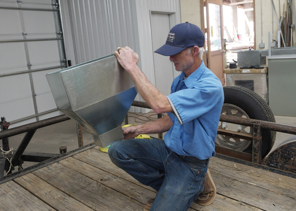 An HVAC technician fabricating custom sheet metal ductwork on a trailer for Carlsbad Heating & Cooling in Carlsbad, NM.