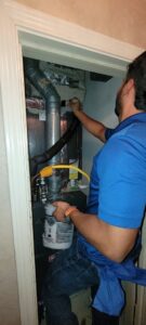 An HVAC technician performing maintenance on a furnace in a utility closet for Service Champs Heating and Air in Fort Worth, TX.