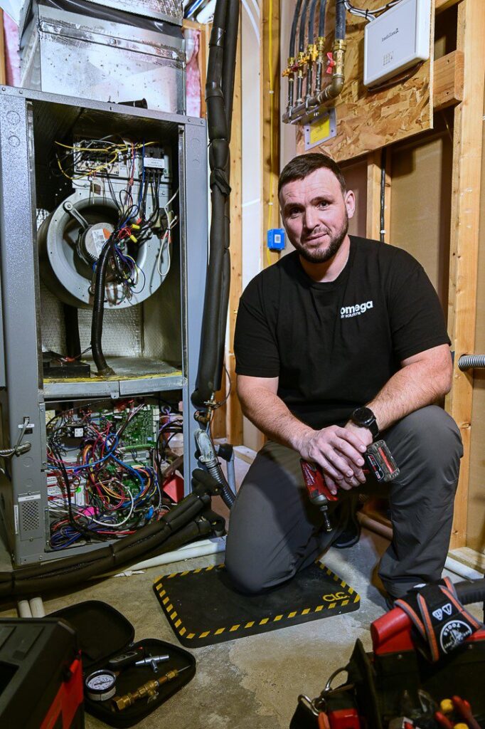 An Omega Air Solutions HVAC technician kneeling next to an open furnace unit, ready for repair in West Des Moines, IA.