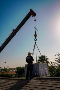 A Lincoln Air & Plumbing technician guiding a large HVAC unit being lowered by a crane onto a rooftop in Phoenix, AZ