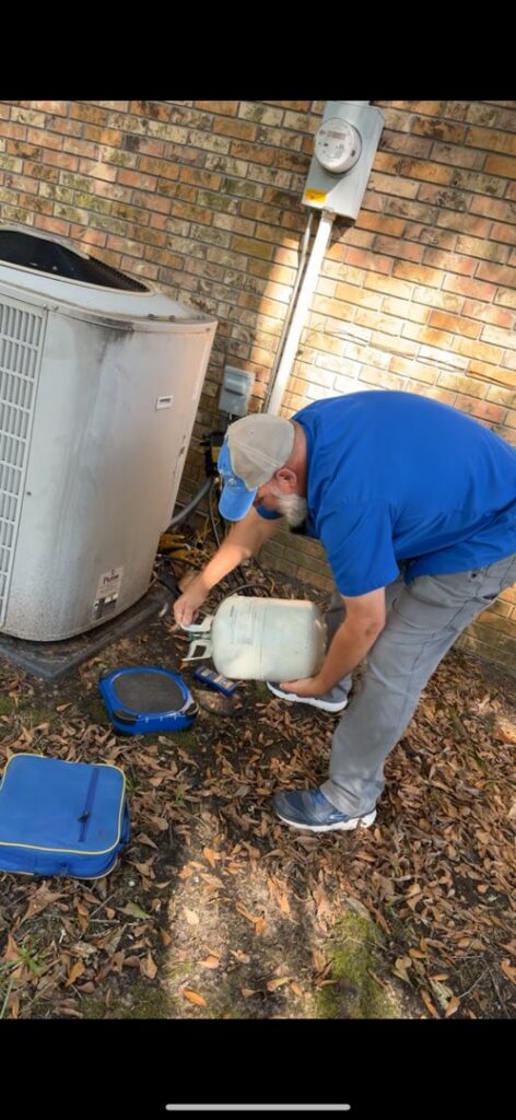 An ARKLA AIR LLC technician handling a refrigerant tank during an HVAC service job near an outdoor AC unit in Springhill, LA.