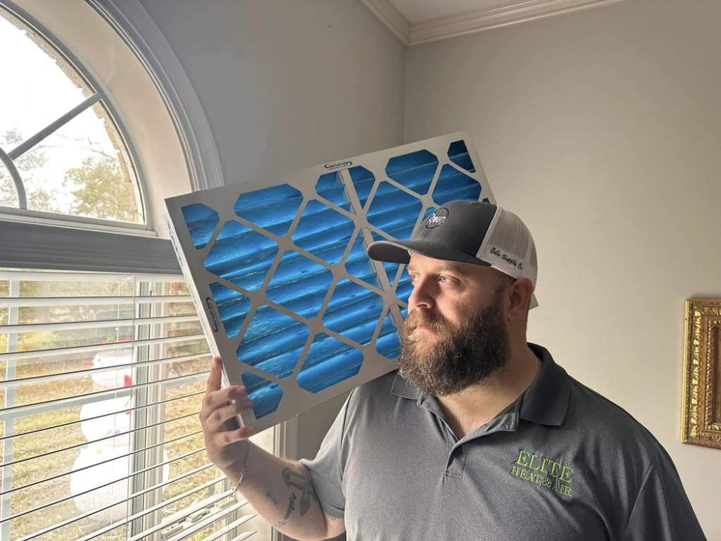 An HVAC technician from Elite Heat & Air in Monroe, LA, holding a new air filter for installation.
