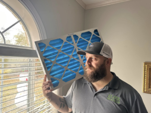 An HVAC technician from Elite Heat & Air in Monroe, LA, holding a new air filter for installation.