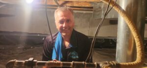 A Precision Vac HVAC technician smiling while working in a crawl space in Thornton, CO.