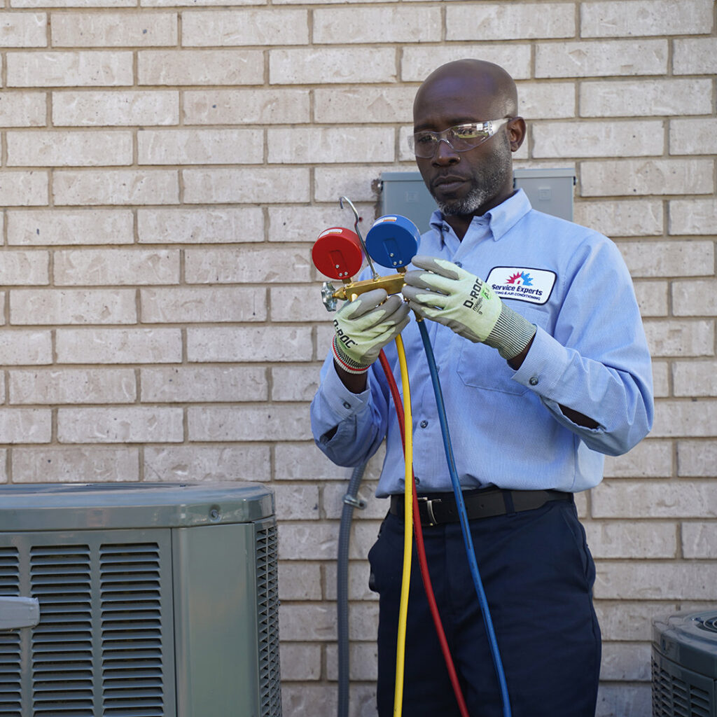 An HVAC technician from Chief/Bauer Service Experts inspecting an outdoor AC unit with manifold gauges in Champaign, IL.