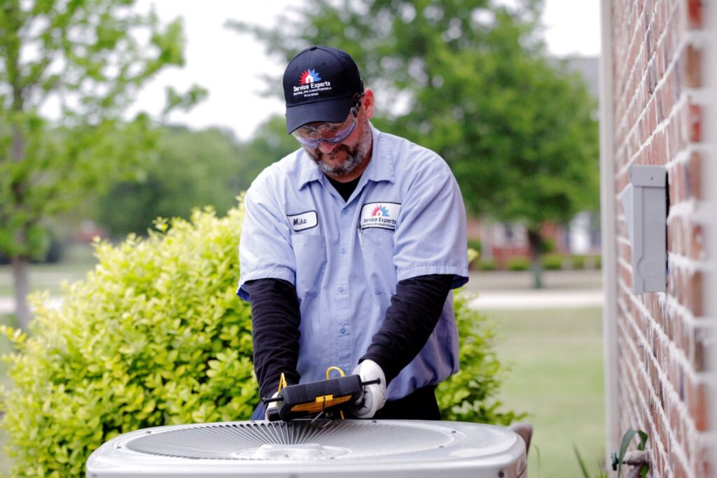 An HVAC technician from Peitz Service Experts inspecting an outdoor AC unit with a diagnostic tool in Pierre, SD.