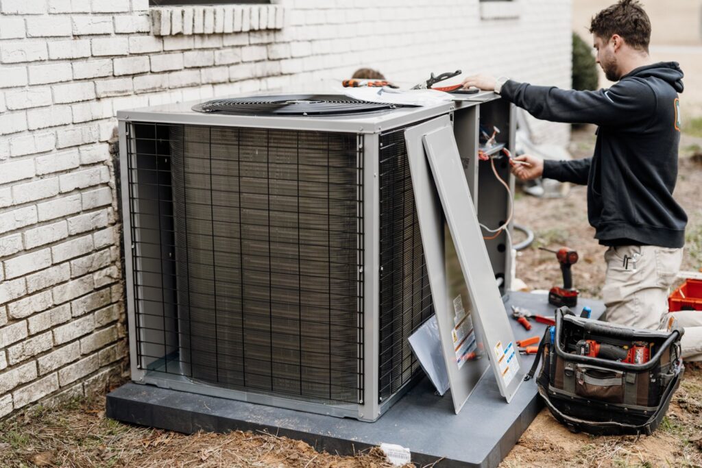 An HVAC technician inspecting an outdoor air conditioning unit with tools for Wingman Heating + Cooling in Auburn, AL.