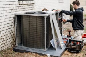 An HVAC technician inspecting an outdoor air conditioning unit with tools for Wingman Heating + Cooling in Auburn, AL.