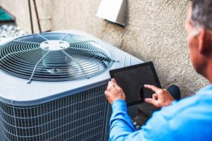 An HVAC technician inspecting an outdoor air conditioning unit with a tablet for Baker Heating & Cooling in Dayton, OH.