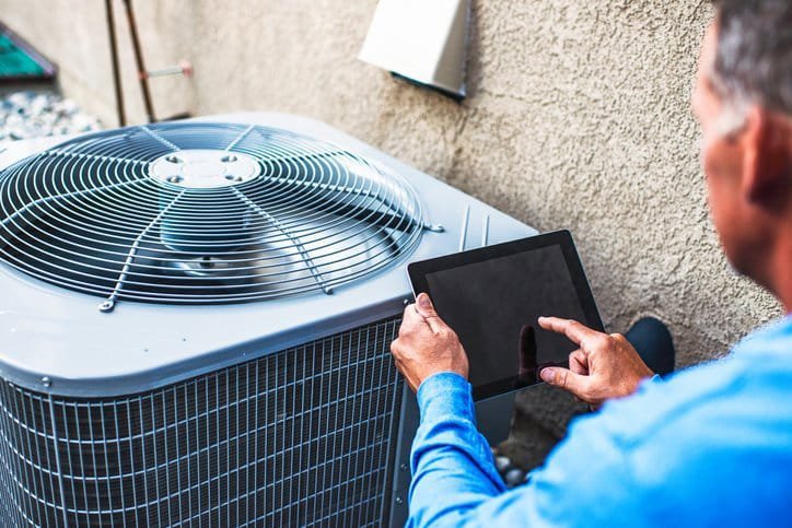 An HVAC technician inspecting an outdoor air conditioning unit with a tablet for Baker Heating & Cooling in Dayton, OH.