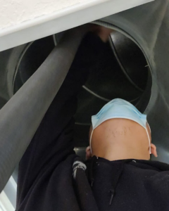 An HVAC technician wearing a mask, inspecting the interior of an air duct for KAP'S HVAC in Portland, OR.