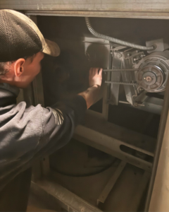 An HVAC technician inspecting the internal components of an air handler or furnace for Climate Systems, Inc. in Sioux Falls, SD.