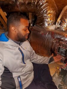 An HVAC technician from Nashville Solutions inspecting an air scrubber device connected to ductwork in an attic in Nashville, TN