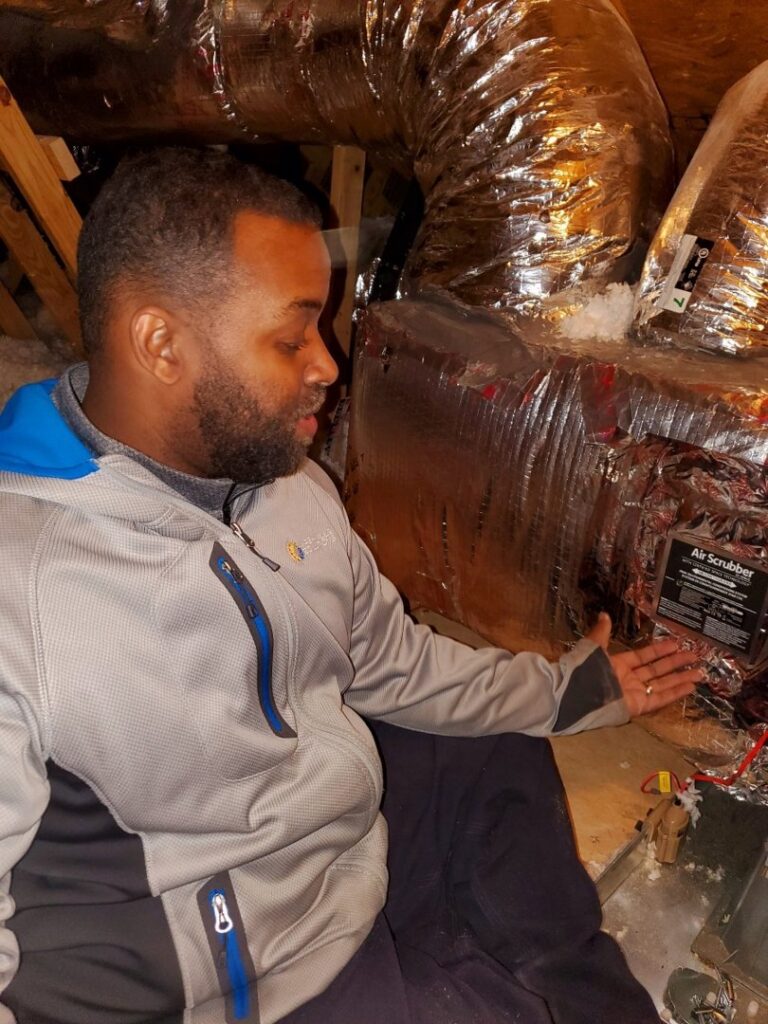 An HVAC technician from Nashville Solutions inspecting an air scrubber device connected to ductwork in an attic in Nashville, TN
