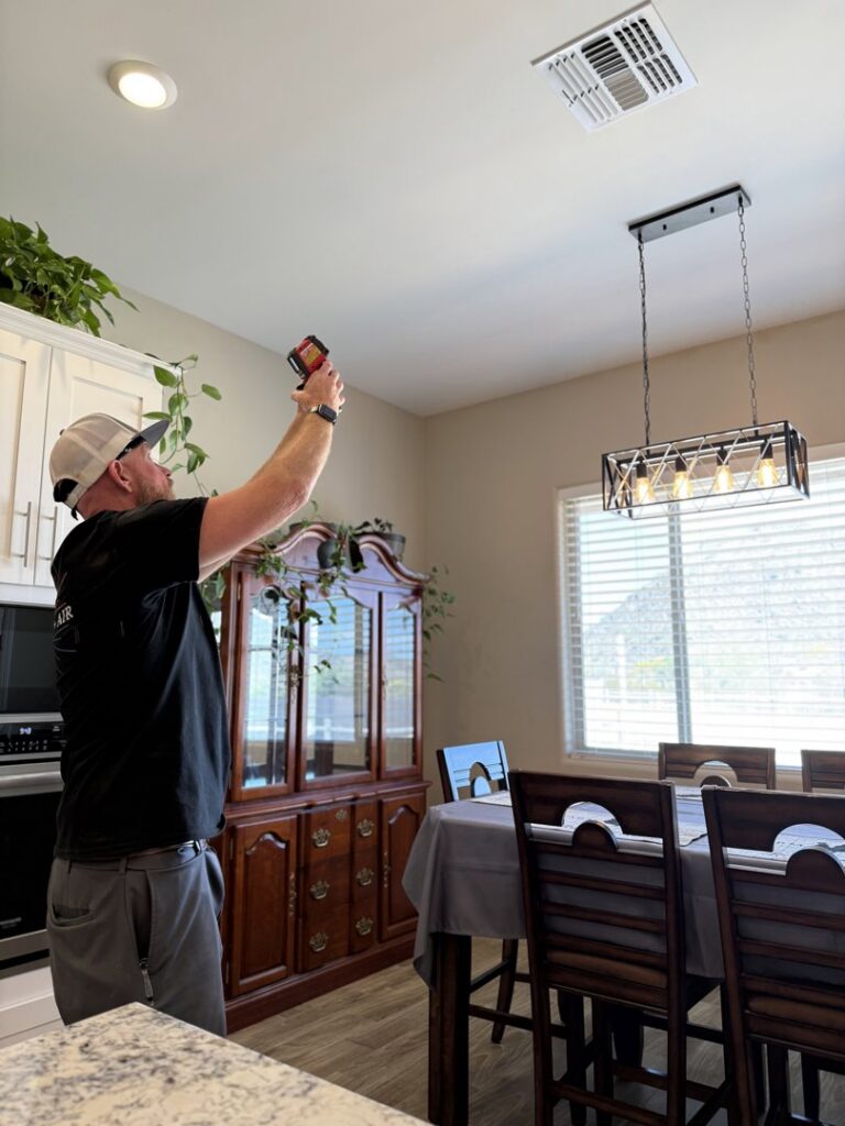 An HVAC technician from TK Heating and Air, PLLC inspecting an indoor air vent with a tool in a home in Queen Creek, AZ