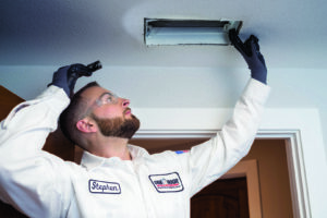An HVAC technician inspecting a ceiling air vent with a flashlight at a client's home for One Hour Heating & Air Conditioning of Albany in Albany, NY